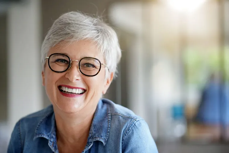 A smiling senior woman with glasses showing a bright, white smile, the kind of result professional teeth whitening delivers, at Copper Sky Dental in Peoria, AZ